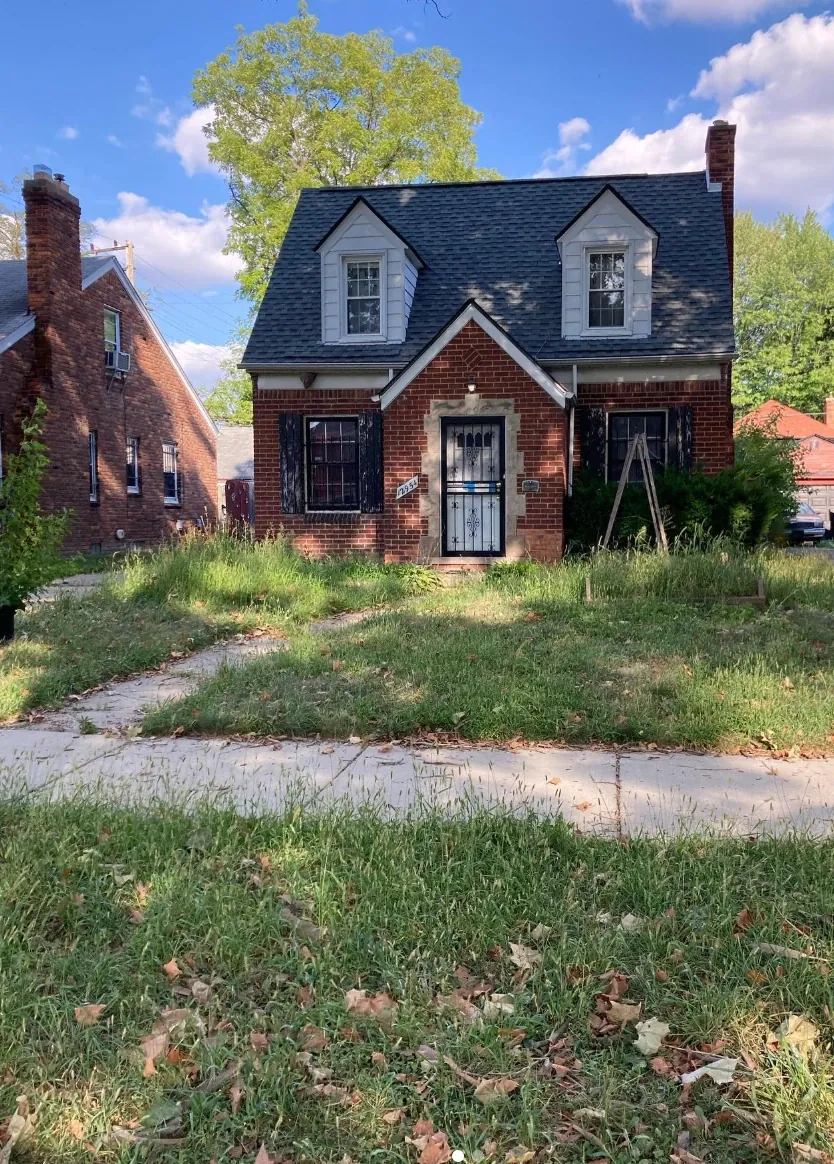 Brick colonial home before service, with an overgrown front lawn covered in leaves and tall grass