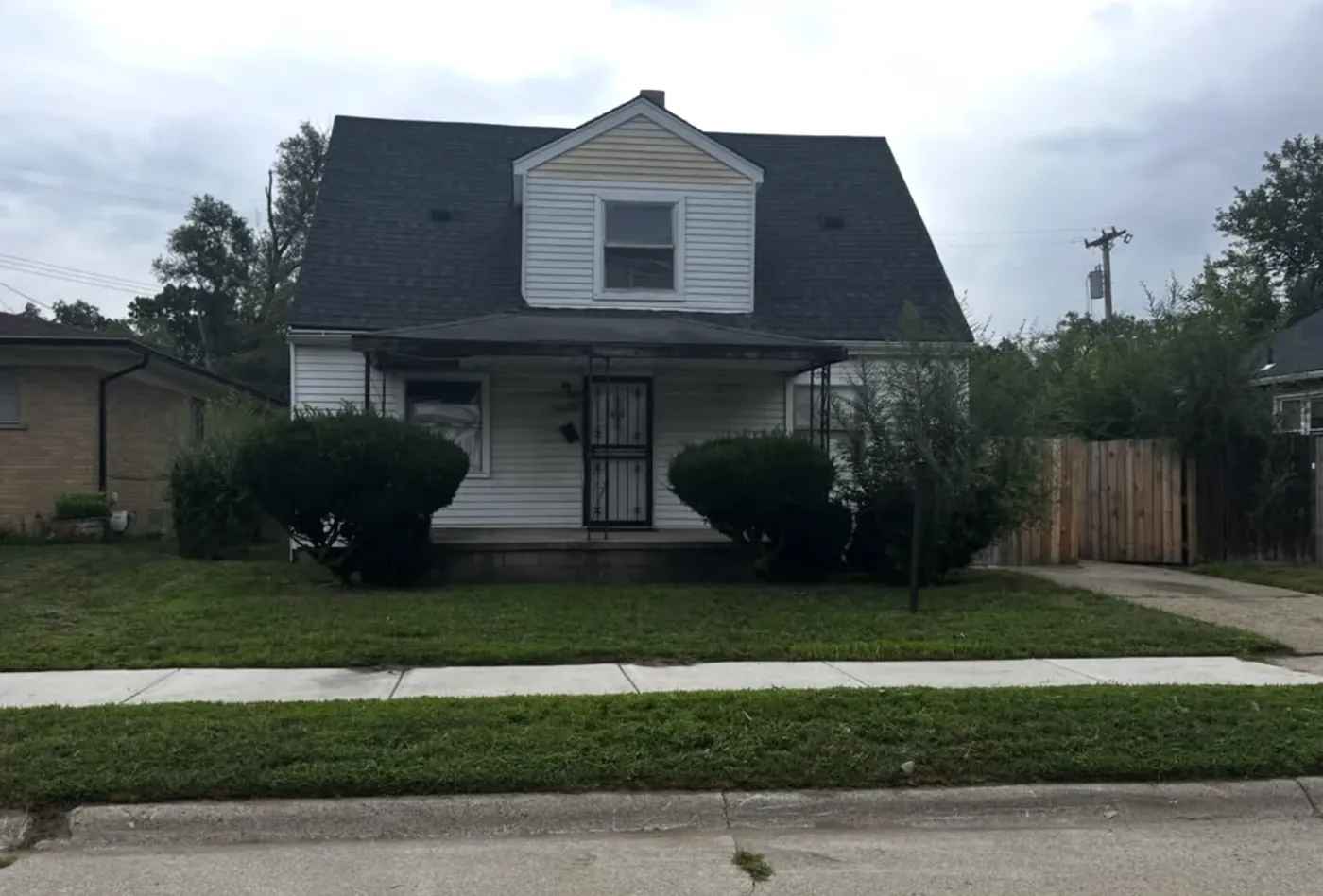 White Cape Cod style home with a freshly mowed front lawn and trimmed shrubs