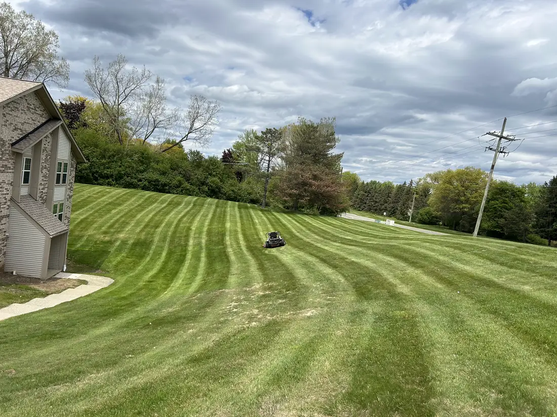 Large property lawn with fresh mowing stripes and a riding mower at work